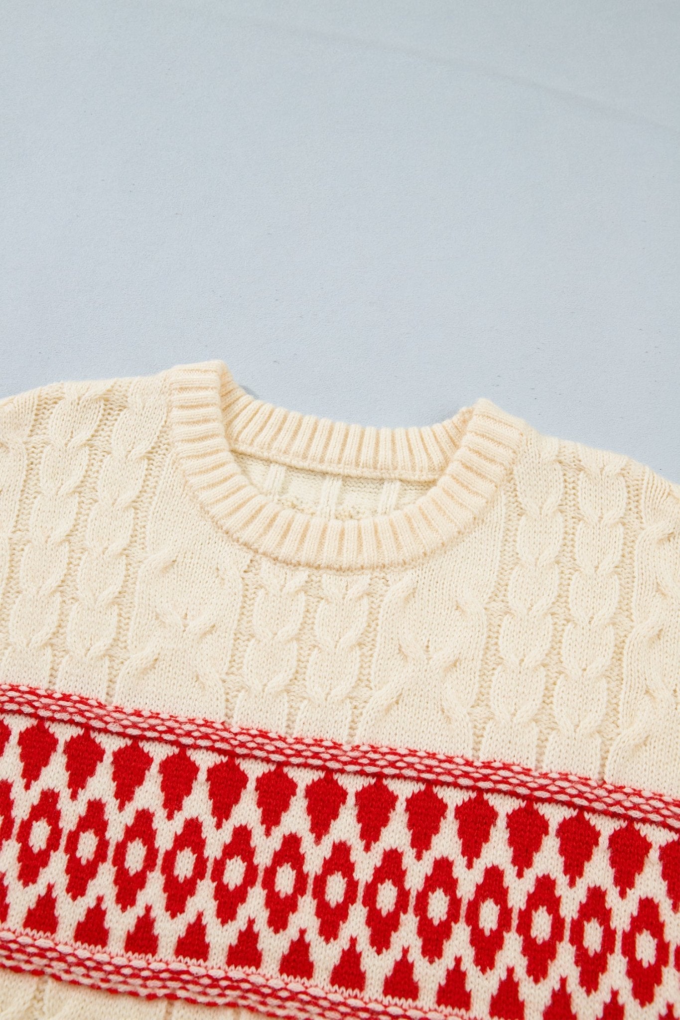 Close-up of cream cable-knit sweater with red geometric patterned chest band.