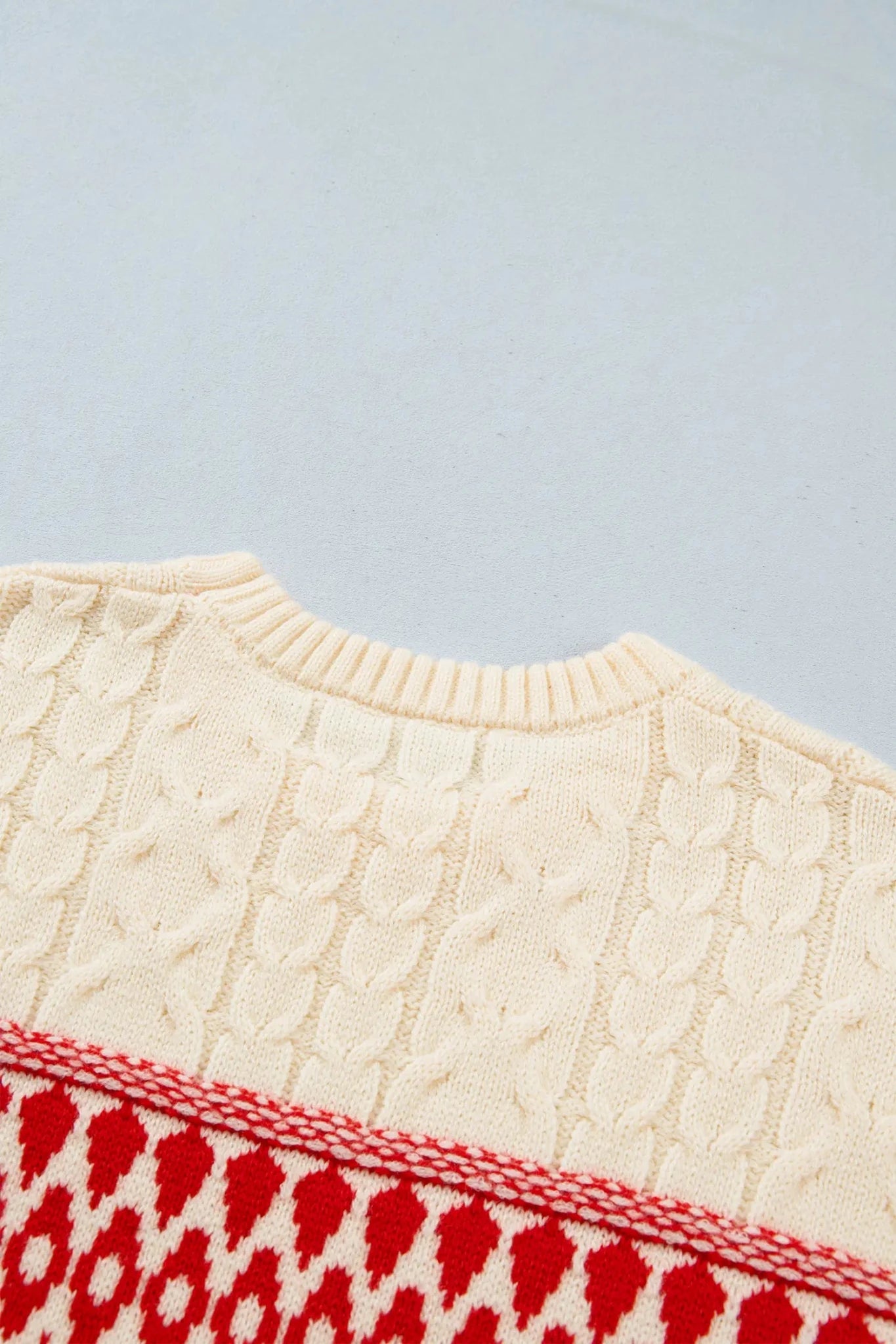 Close-up of cream cable-knit sweater with red geometric hem border.
