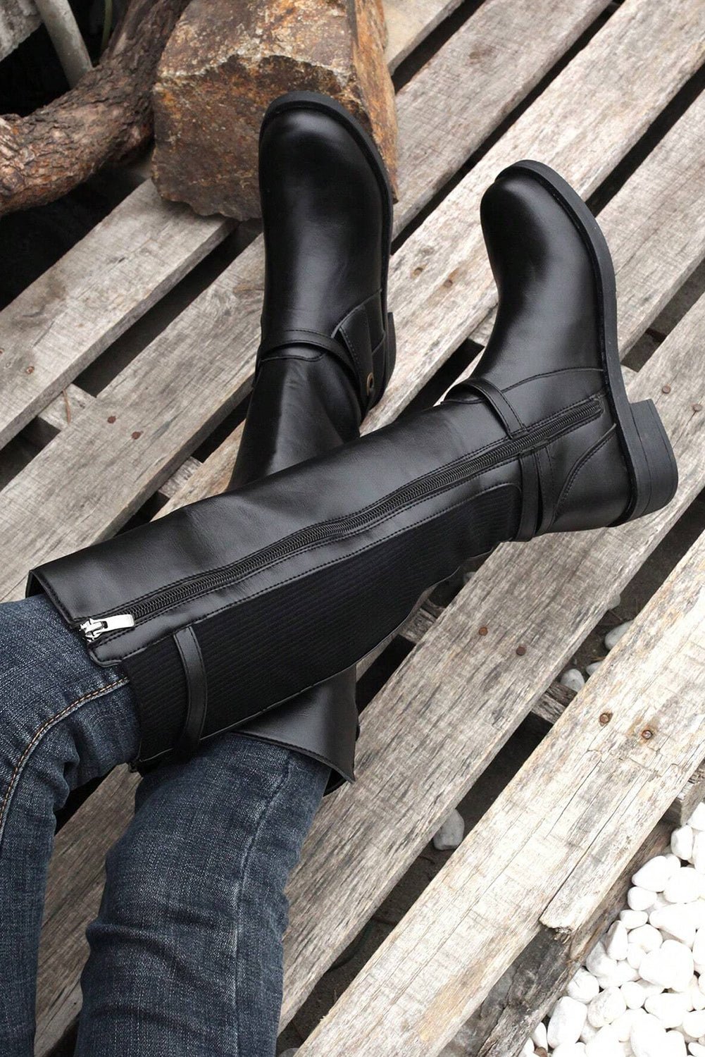 Black knee-high boots worn by a person on a wooden surface.