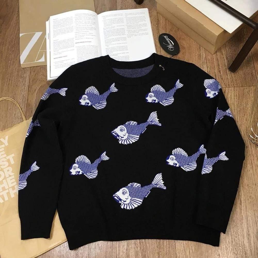 Black sweater with blue fish patterns on a wooden floor with books and a bag.