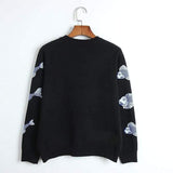 Black sweater with fish patterns on sleeves, hanging on a wooden hanger against a white background.