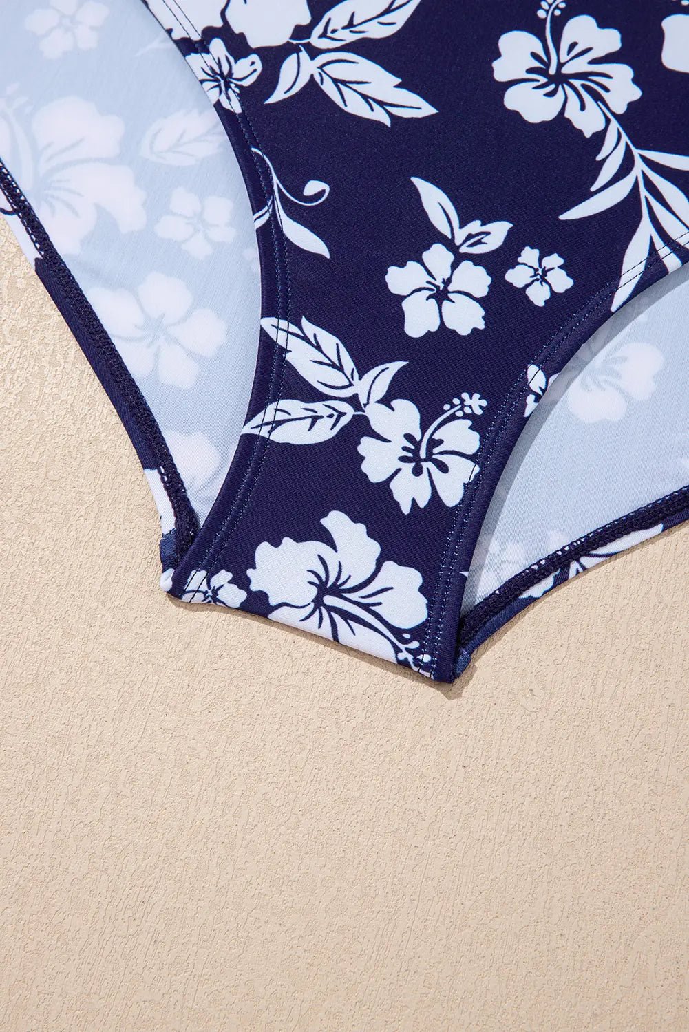 Navy blue swimsuit with white floral pattern on a beige background