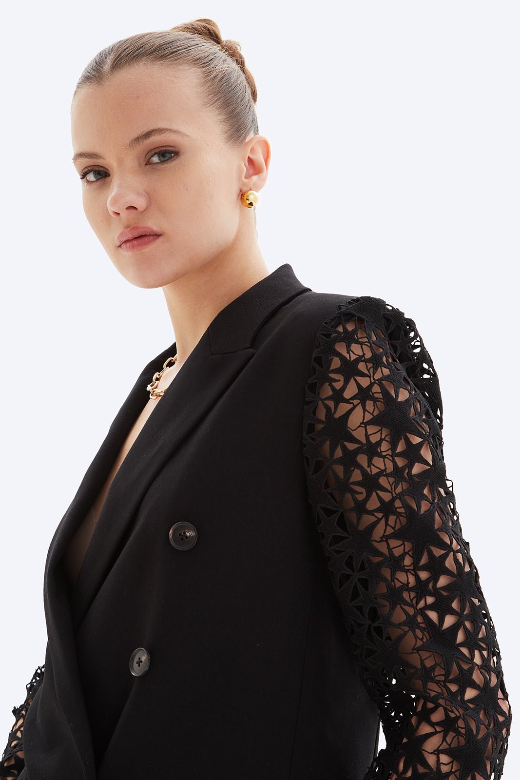 Woman wearing a black blazer with lace sleeves on a white background