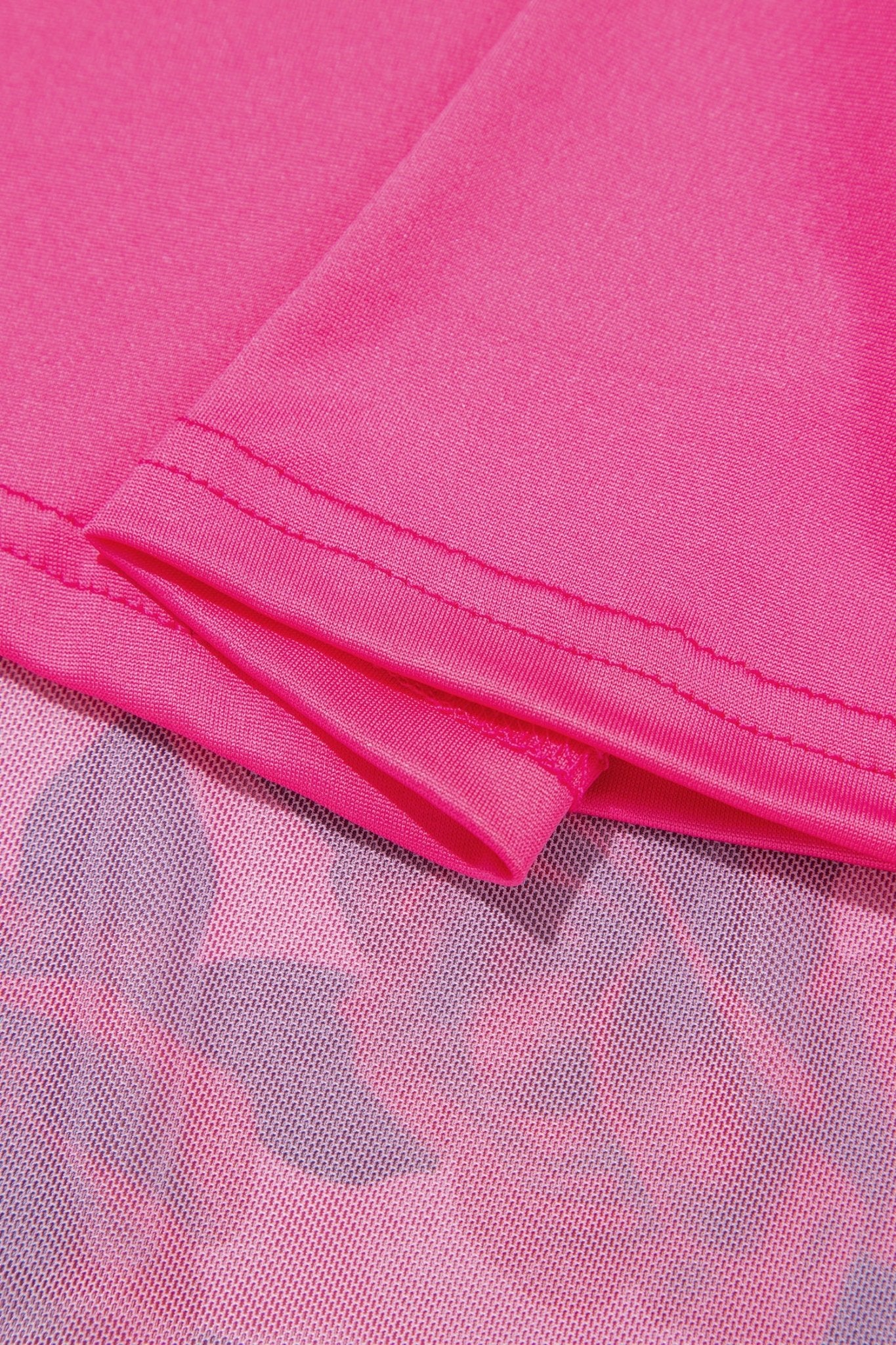 Close-up of a bright pink garment fabric with a folded hem and a sheer floral mesh layer underneath.