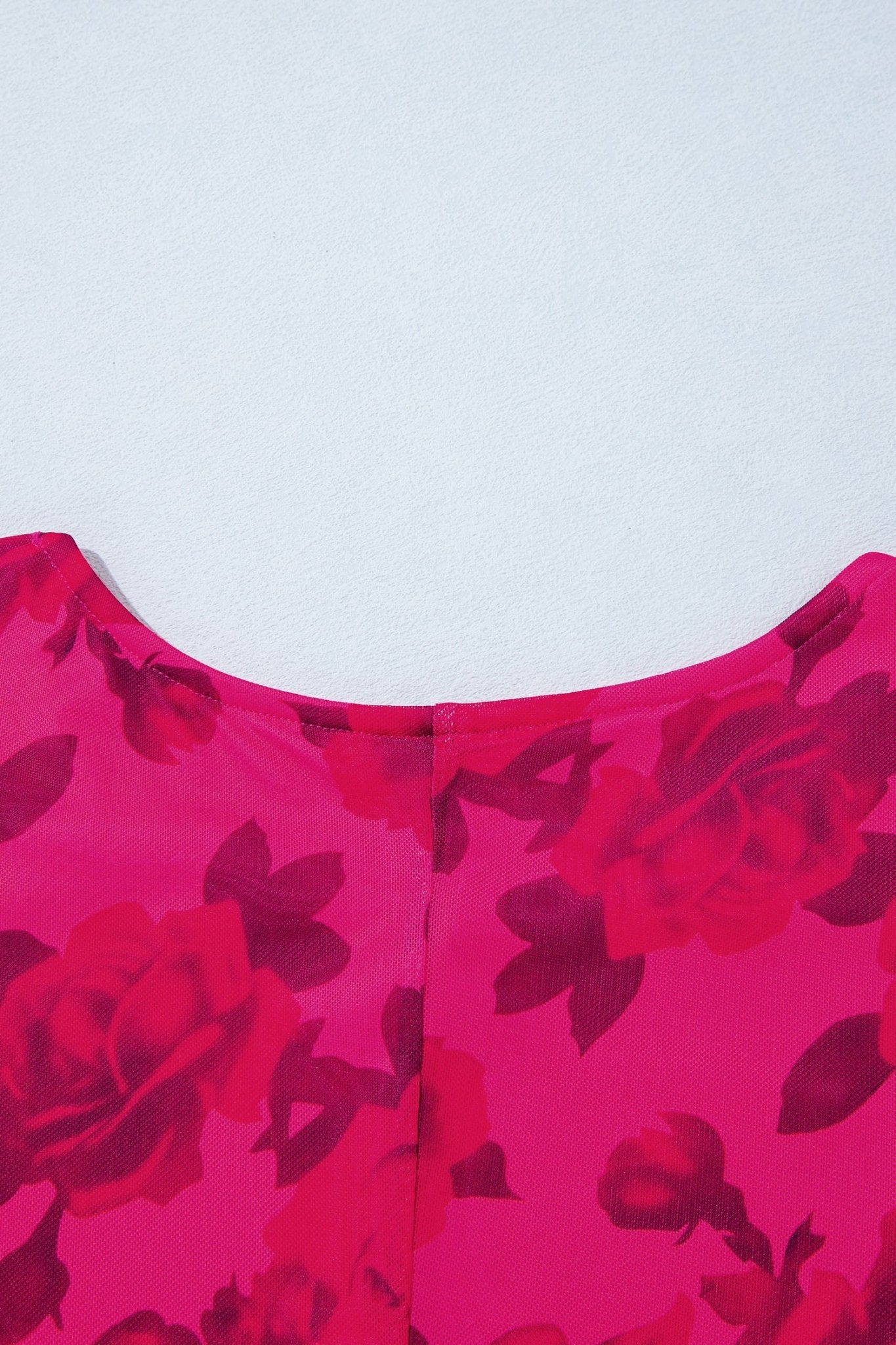 Close-up of bright pink garment with dark red rose print, showing neckline and center seam against light gray.