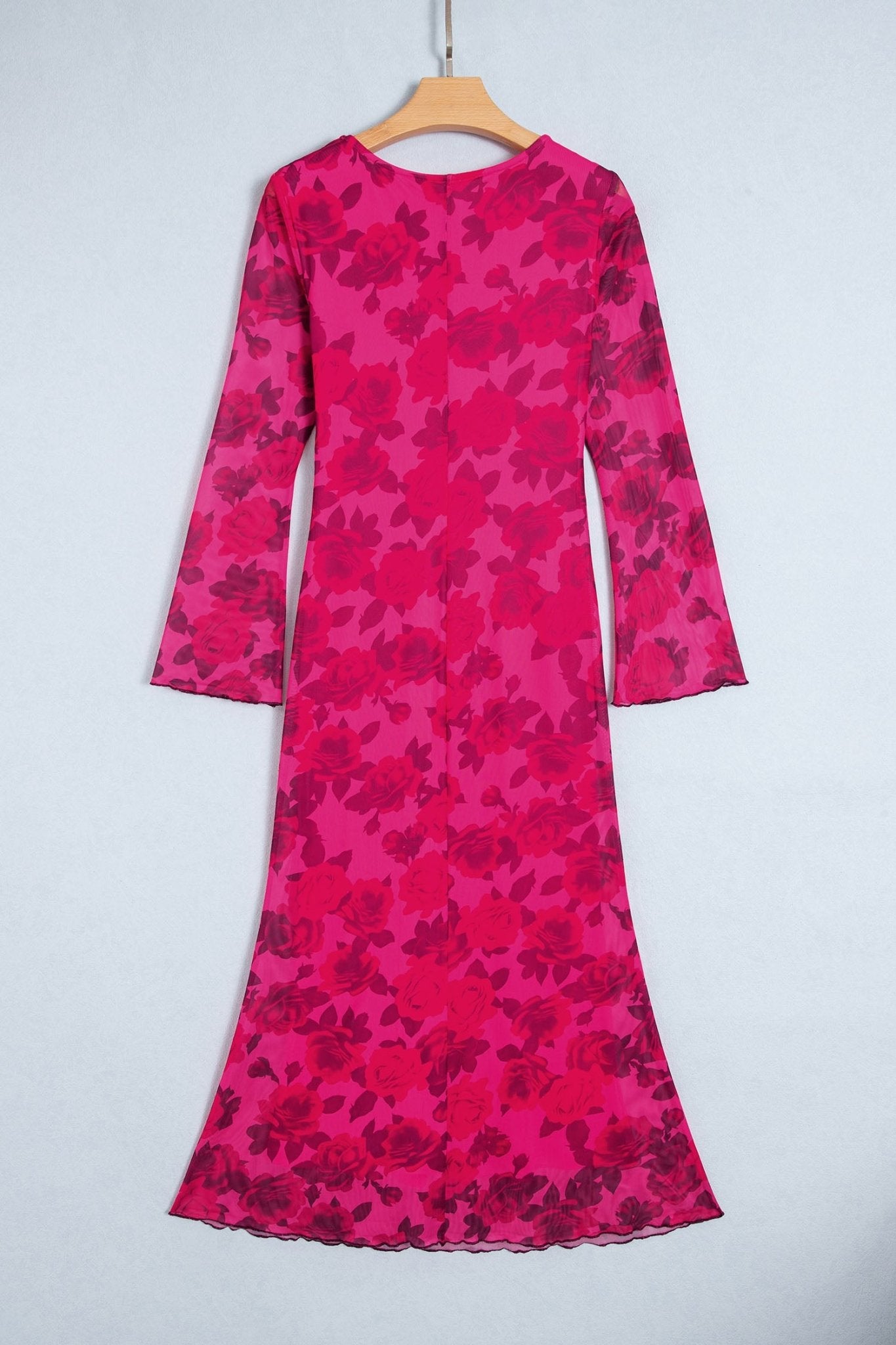 Vibrant pink long-sleeve midi dress with dark red floral pattern, hanging on a wooden hanger against light gray.