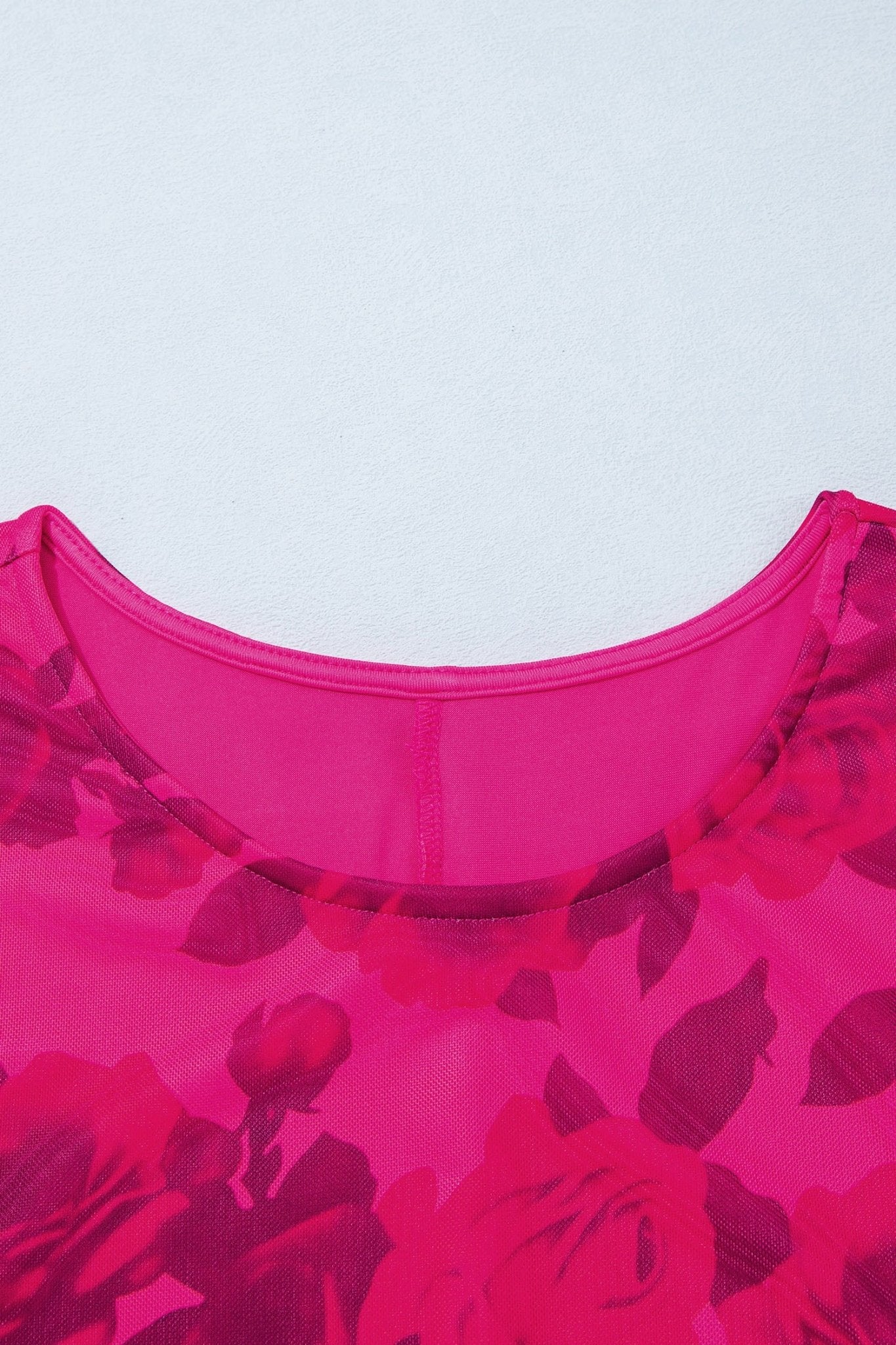 Close-up of a bright pink top featuring a sheer mesh neckline and a dark pink floral rose pattern.