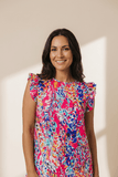 Woman wearing a colorful floral dress against a beige wall