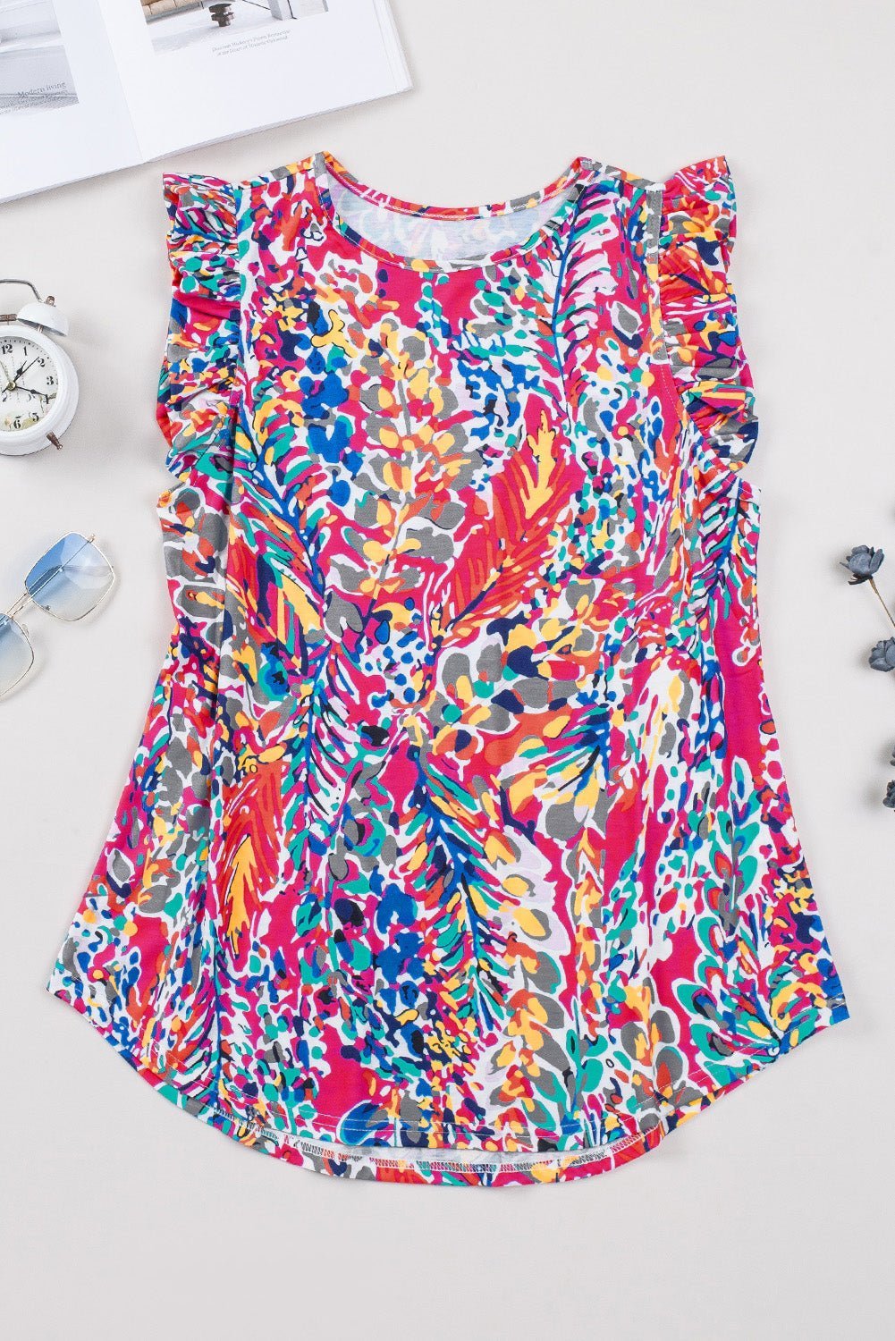 Colorful floral top on a white surface with a clock and water bottle in the background.