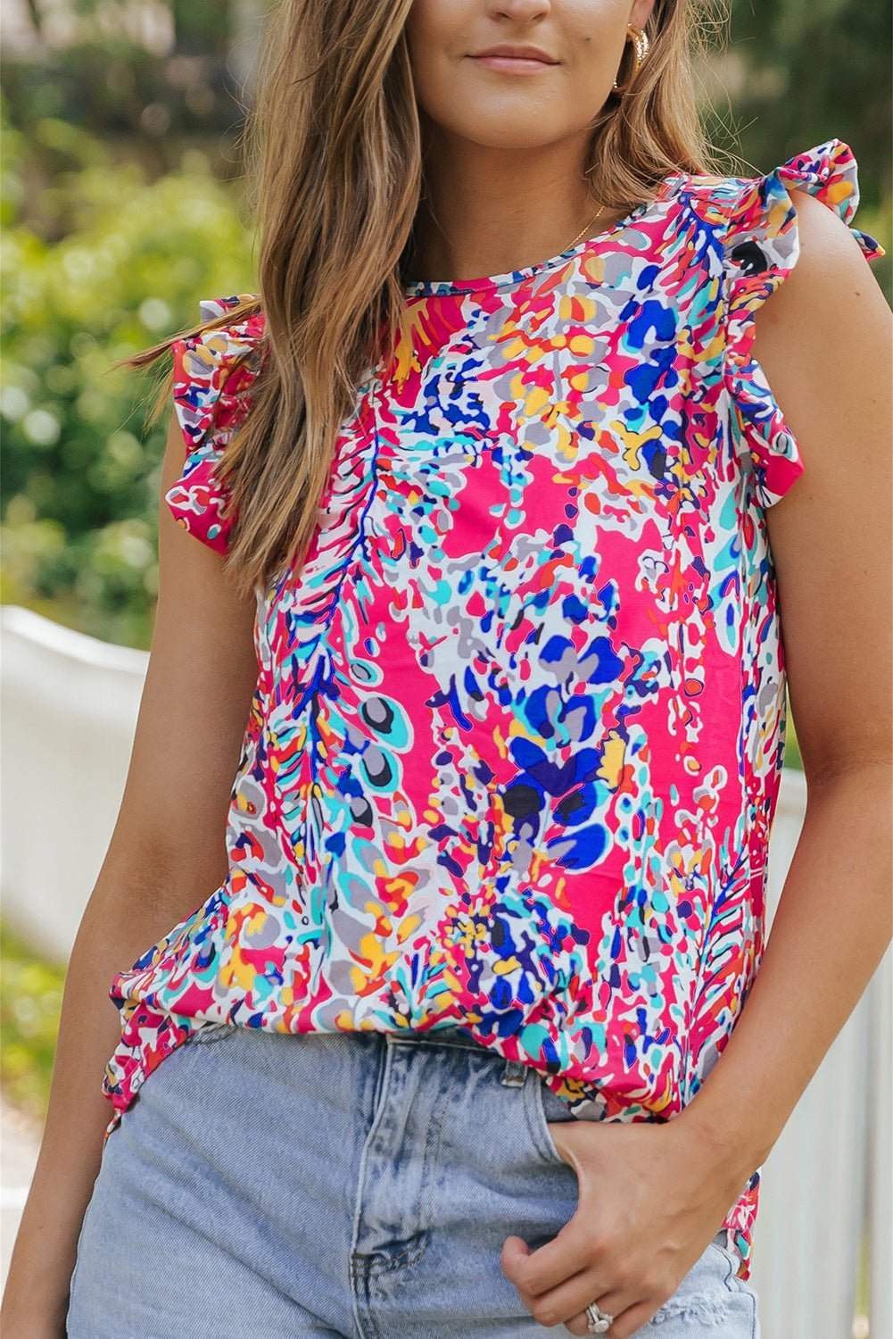 Woman wearing a colorful floral top with ruffled sleeves outdoors.