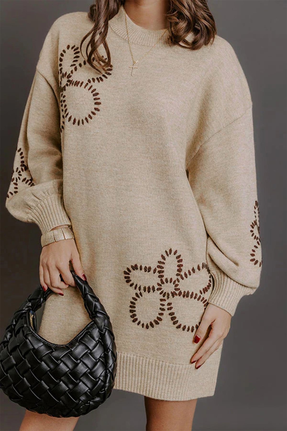 Woman in oversized beige sweater dress with brown floral patterns and black woven bag.