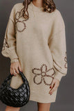 Woman in oversized beige sweater dress with brown floral patterns and black woven bag.