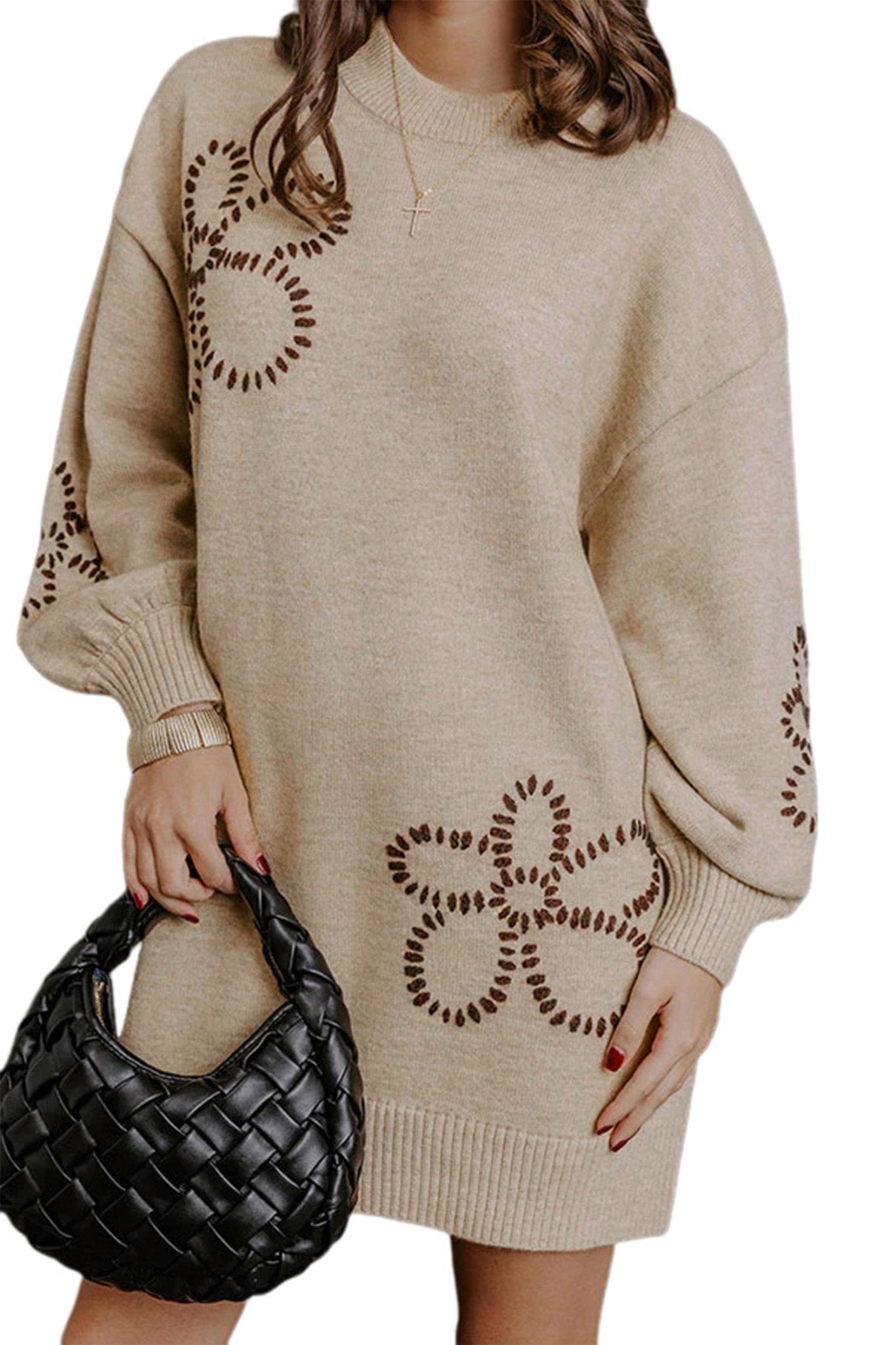 Woman in beige knit sweater dress with brown floral patterns and black woven hanbag.