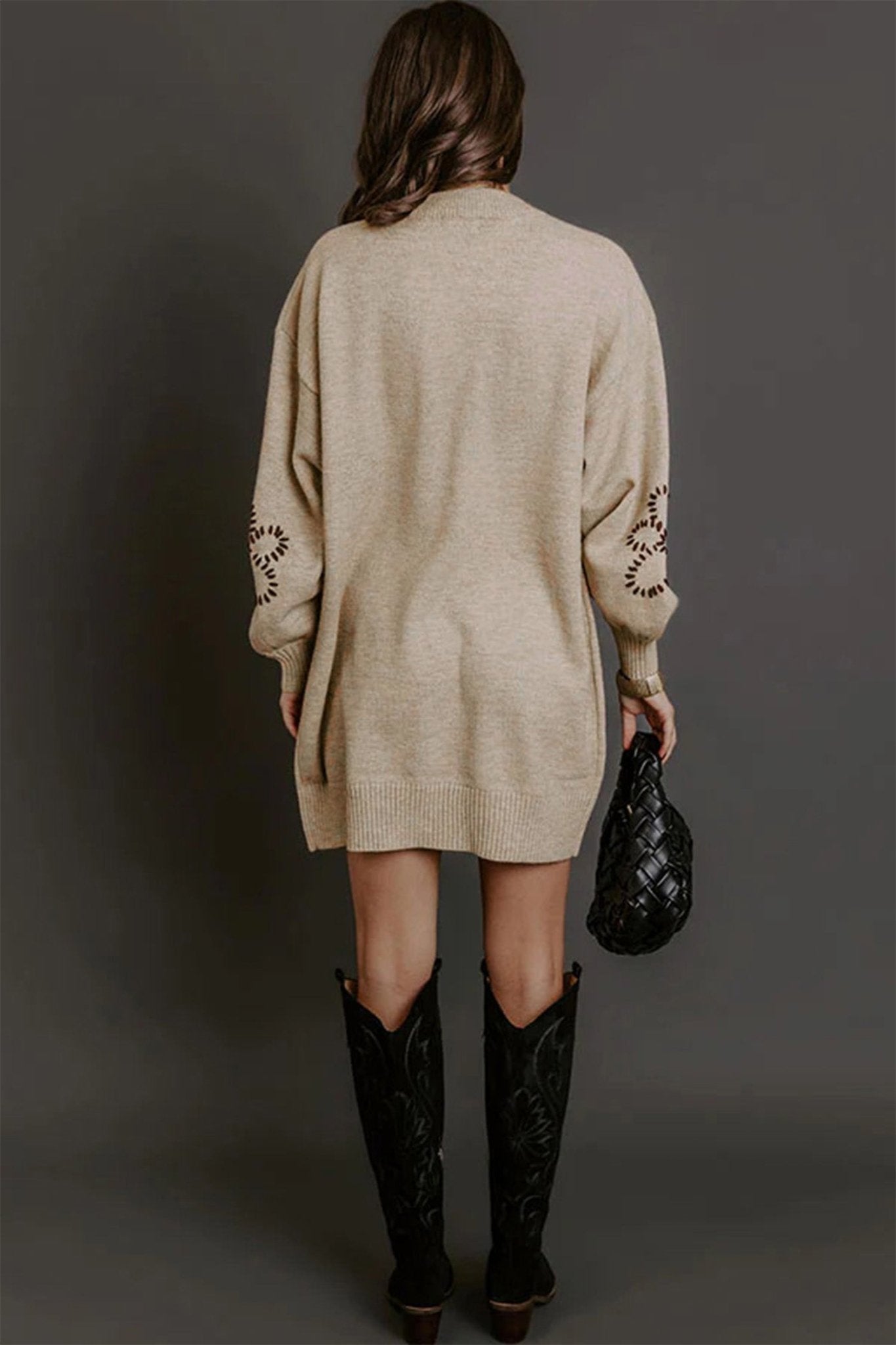 Back view of woman in beige knit sweater dress with cutout sleeves and black boots.
