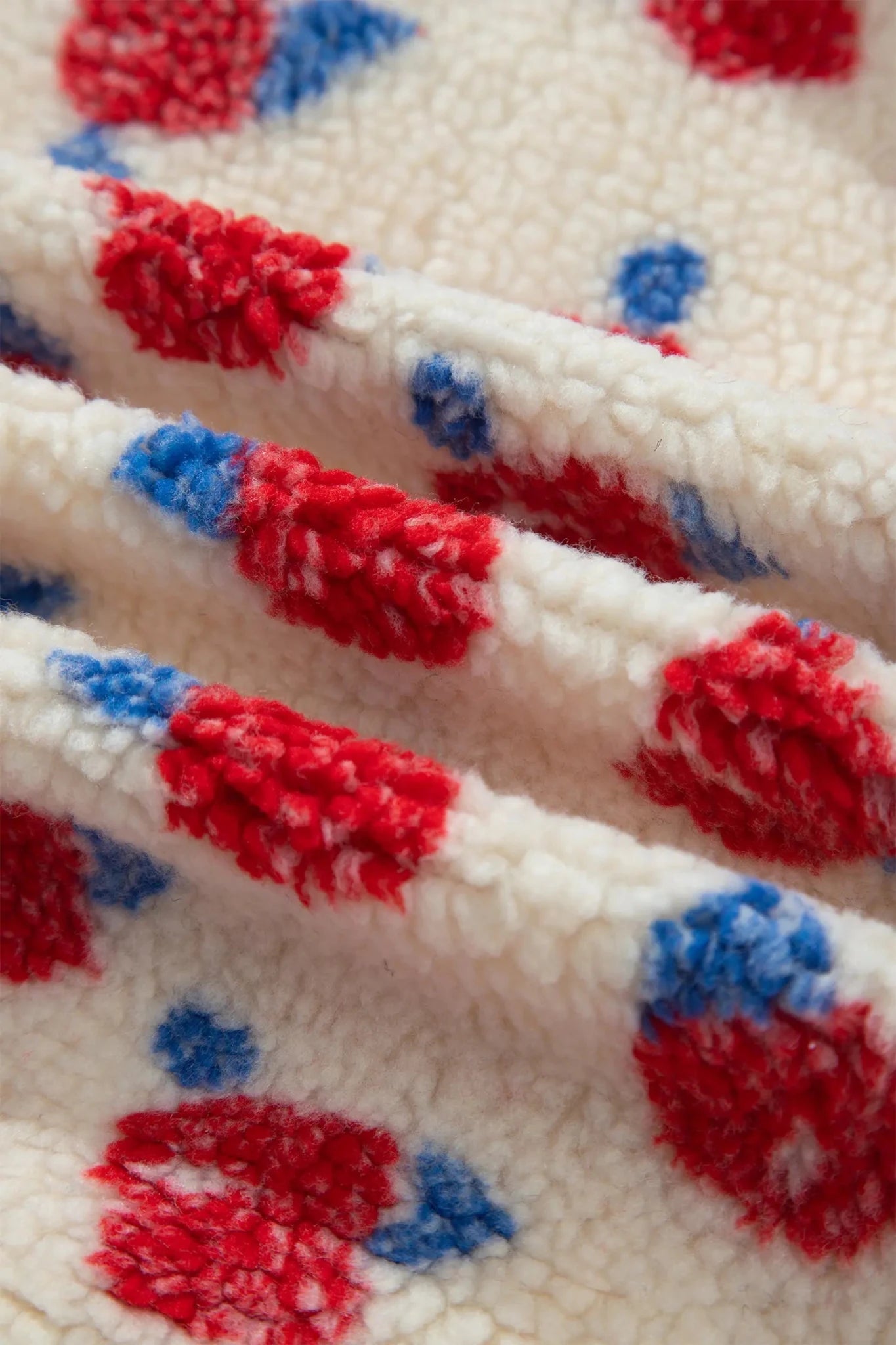 Close-up of a plush sherpa fabric with a red and blue abstract pattern on an off-white background.