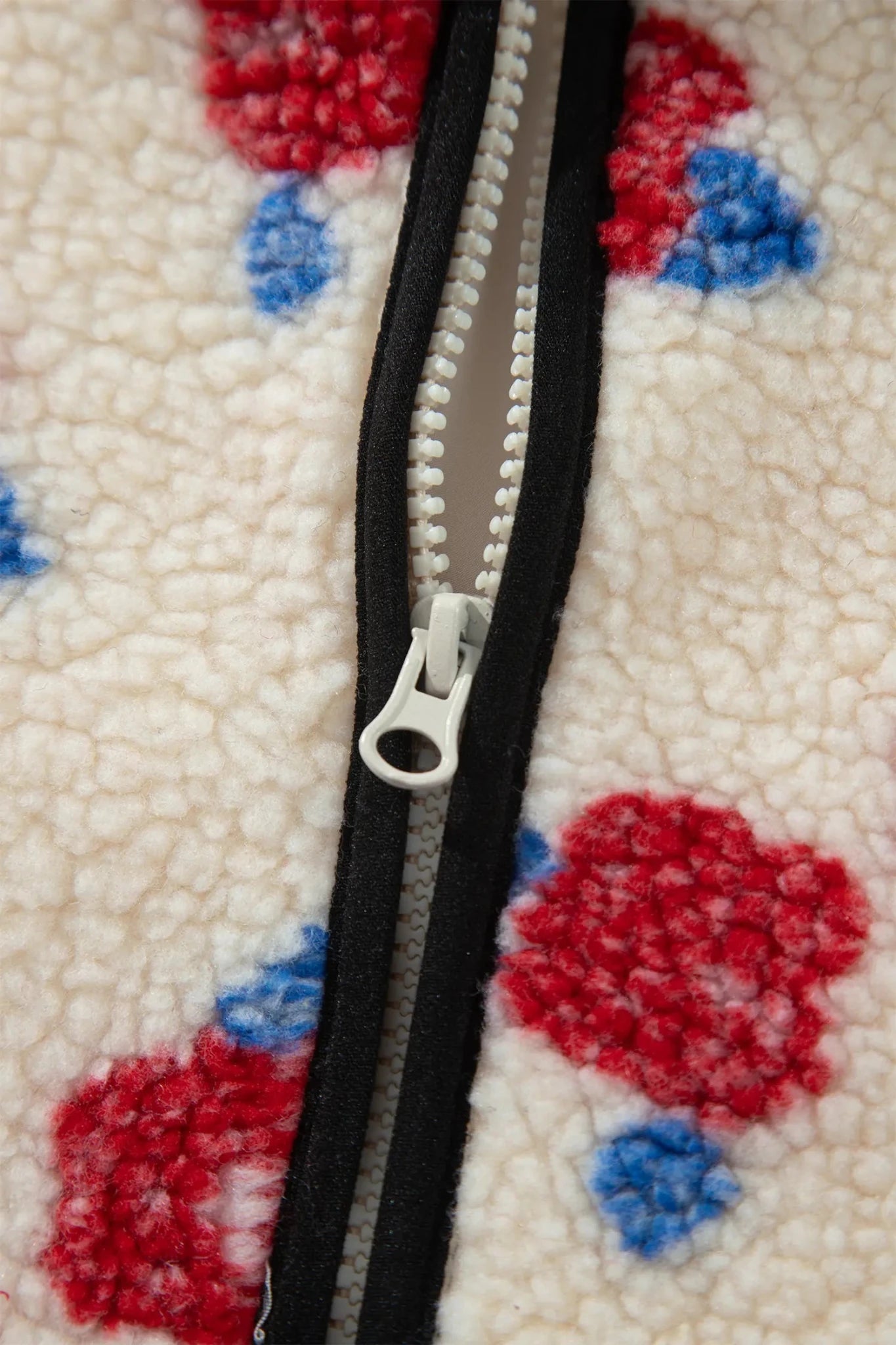 Close-up of a white sherpa fleece jacket with a black zipper and a red and blue floral pattern.