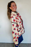 Woman in cream sherpa jacket with red-blue rose print and black trim.
