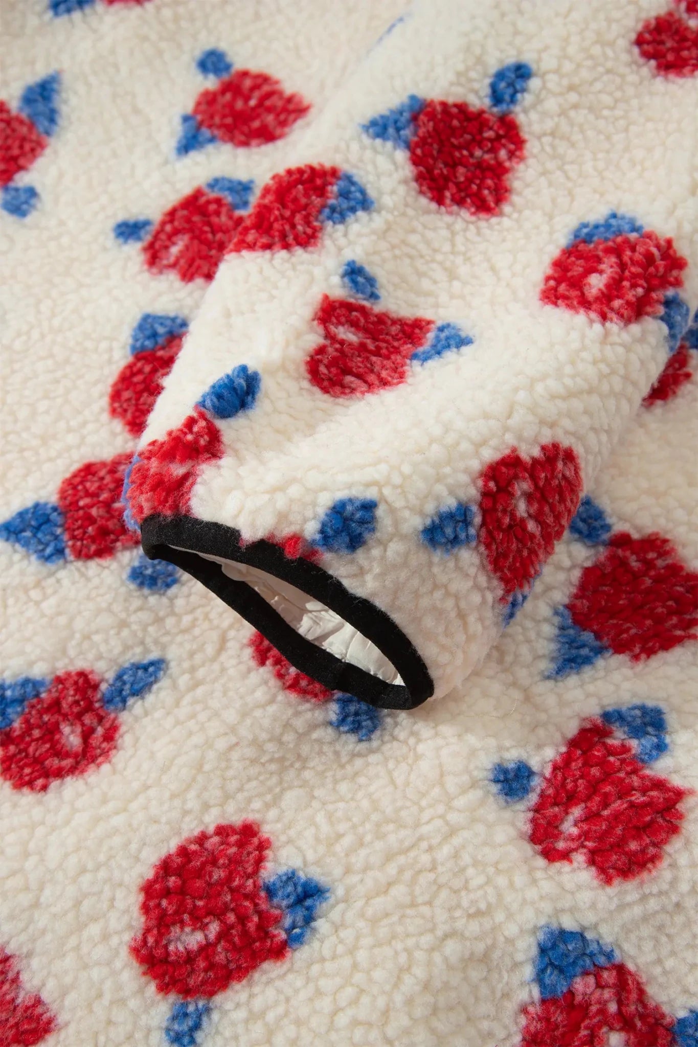 Close-up of cream sherpa fleece with red-blue floral print and black trim.
