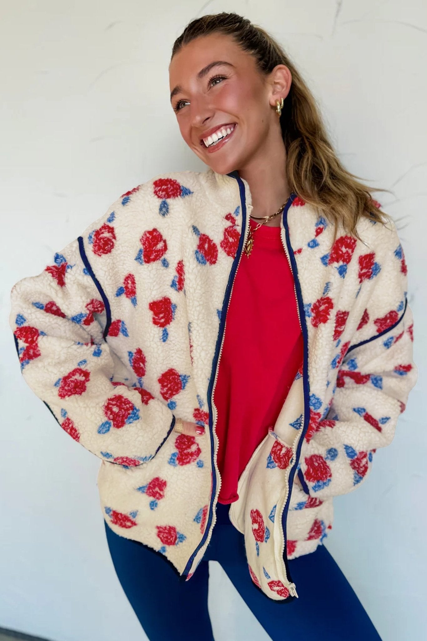 Smiling woman in cream floral sherpa jacket, red top, and blue leggings.