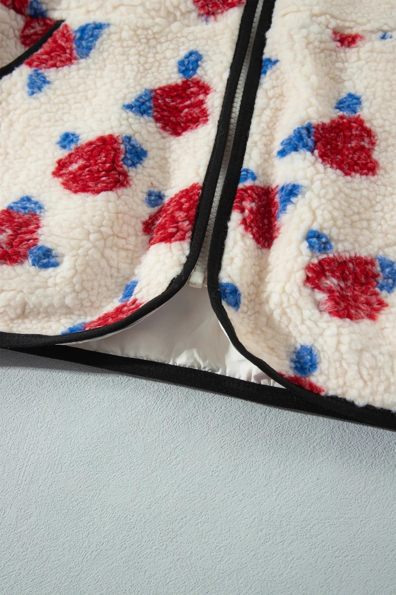 Close-up of cream sherpa fabric with red-blue floral print and black trim.