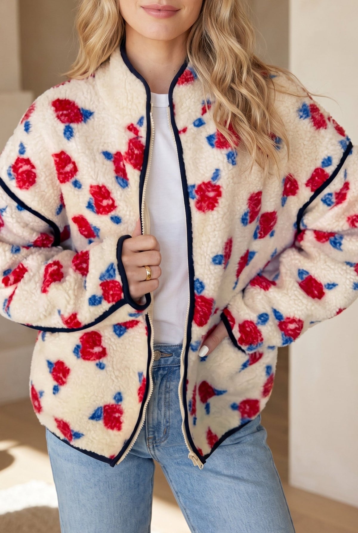 Woman in cream sherpa jacket with red-blue floral print, white top, and jeans.