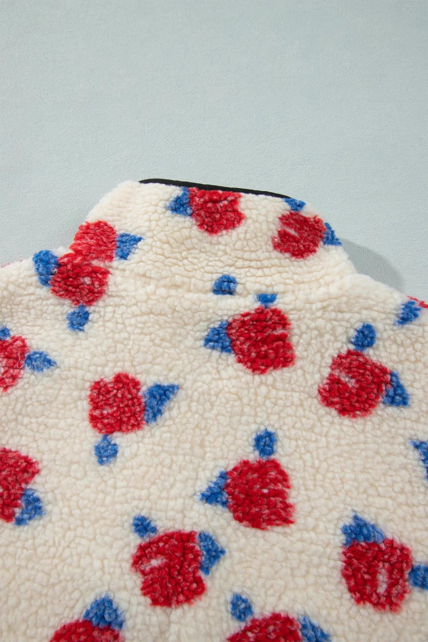 Close-up of cream sherpa fleece with red-blue floral pattern.