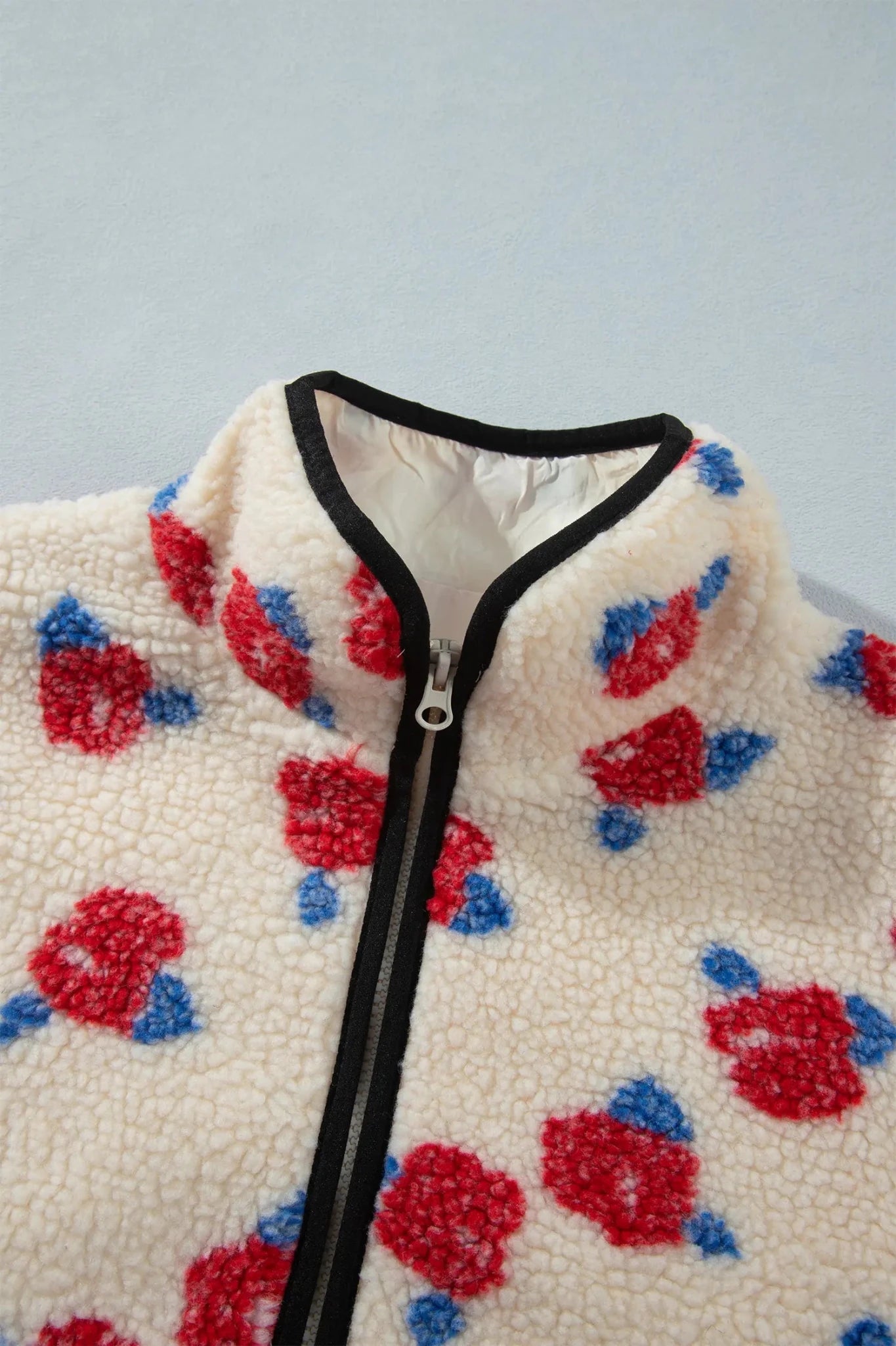 Close-up of cream floral fleece jacket with black trim and zipper.