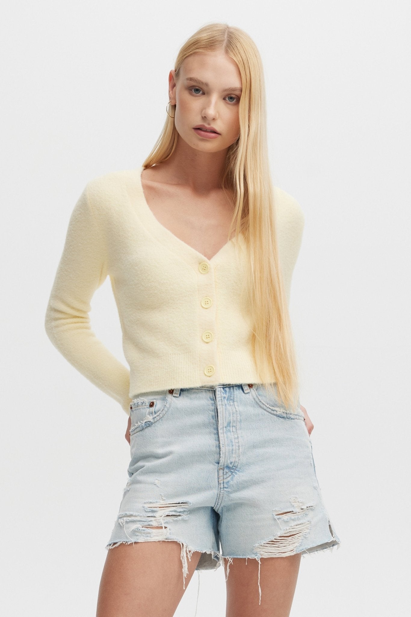 Woman wearing a light yellow cardigan and denim shorts on a white background