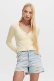 Woman wearing a light yellow cardigan and denim shorts on a white background