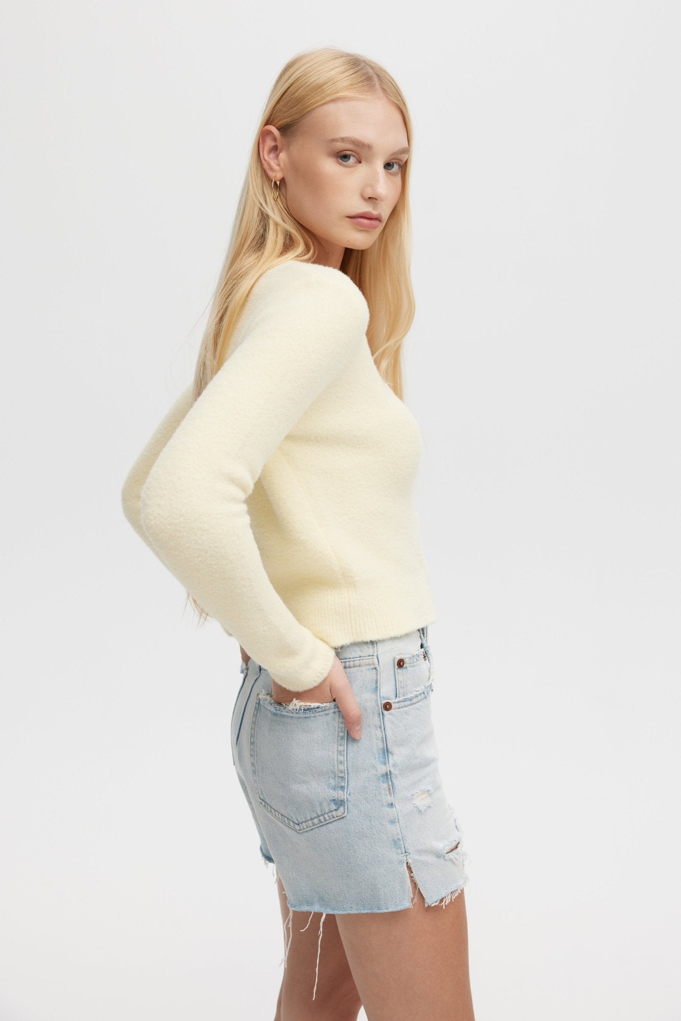 Woman wearing a light yellow sweater and denim skirt on a white background