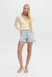 Woman wearing a yellow top and denim shorts on a white background