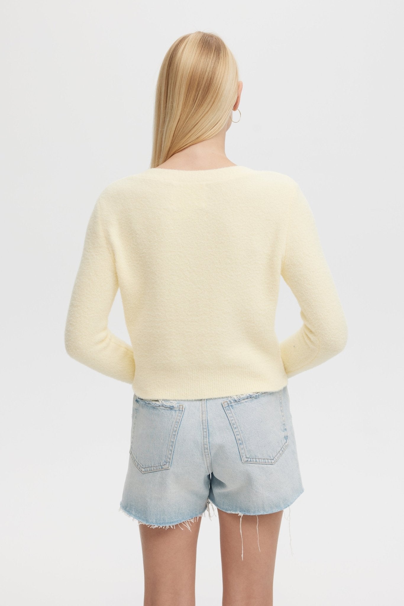 Person wearing a light yellow sweater and denim shorts on a plain background