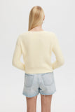 Person wearing a light yellow sweater and denim shorts on a plain background