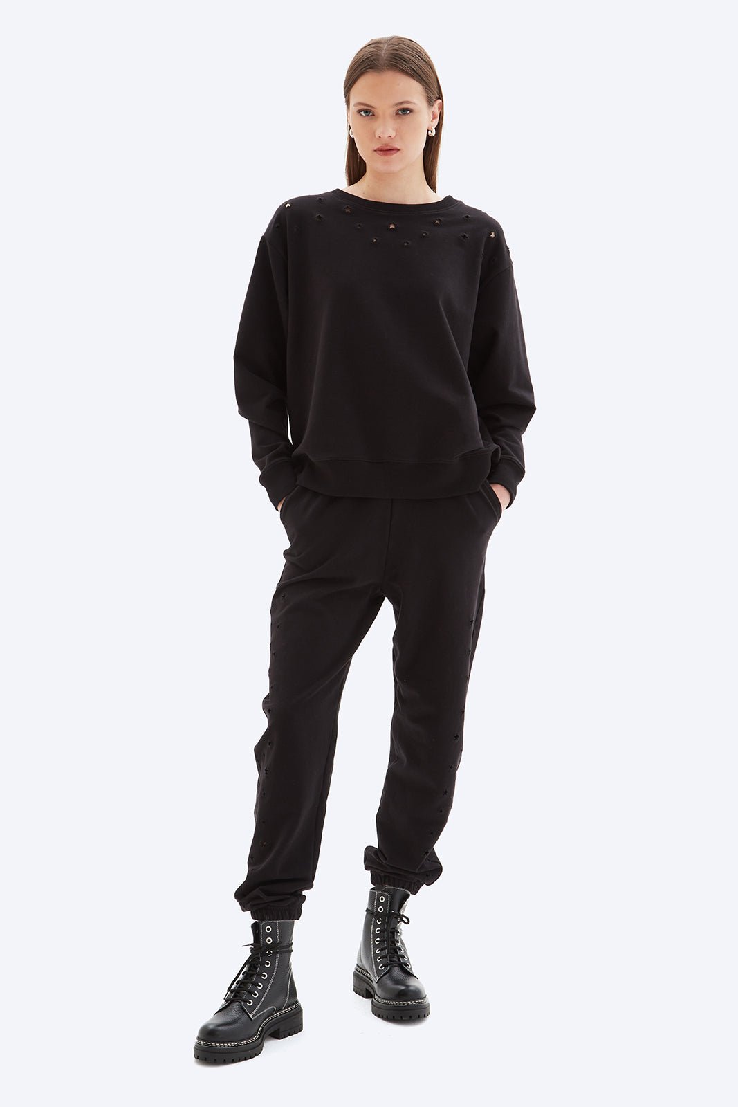 Person wearing a black outfit with black boots on a white background