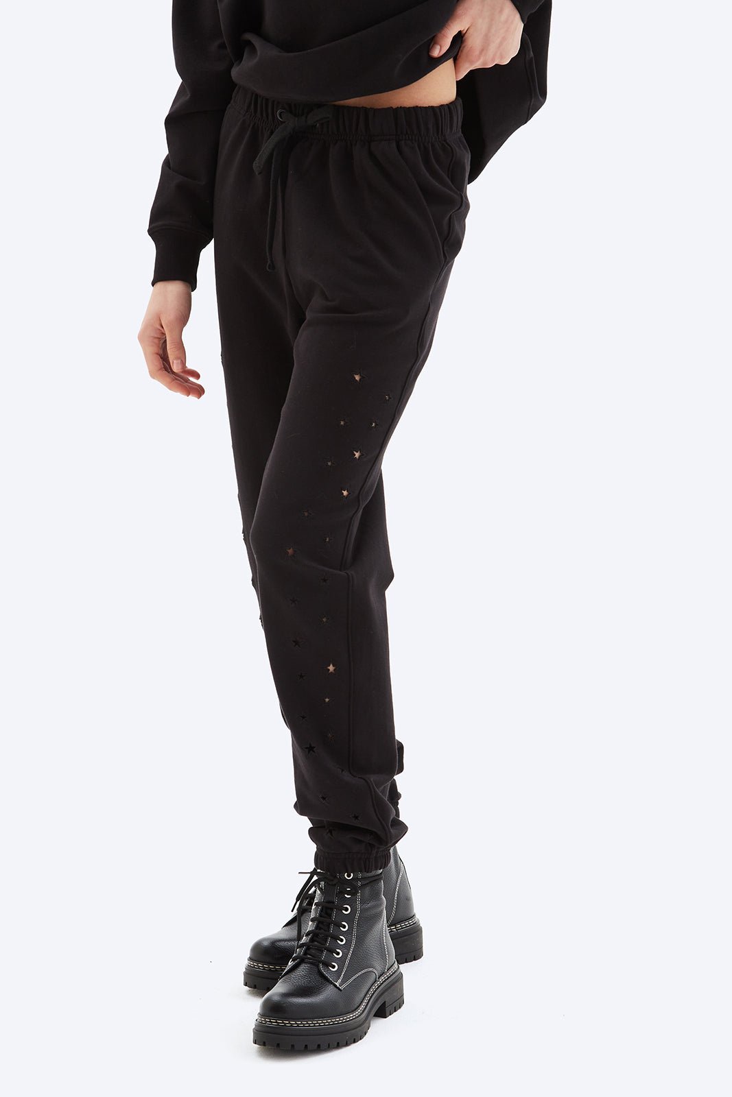 Person wearing black jogger pants and black boots on a white background