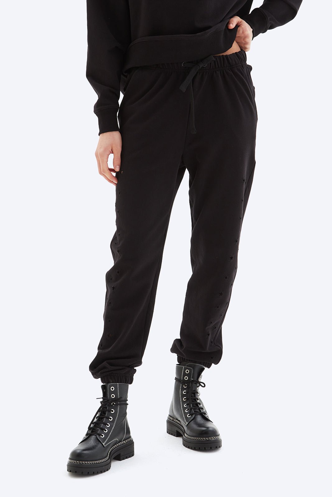 Person wearing black jogger pants and black boots on a white background