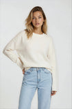Woman wearing a white sweater and light blue jeans against a plain background