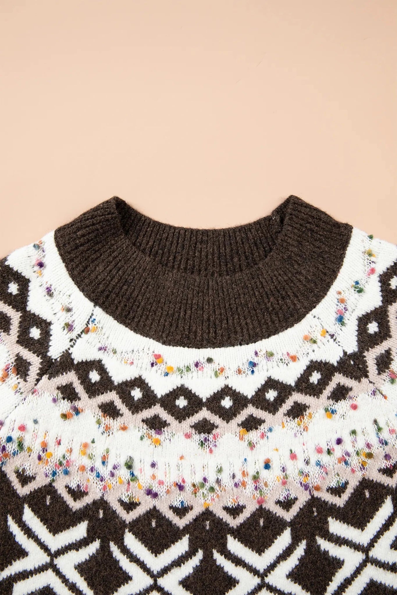 Close-up of a brown knit sweater with white diamond patterns and colorful confetti details.