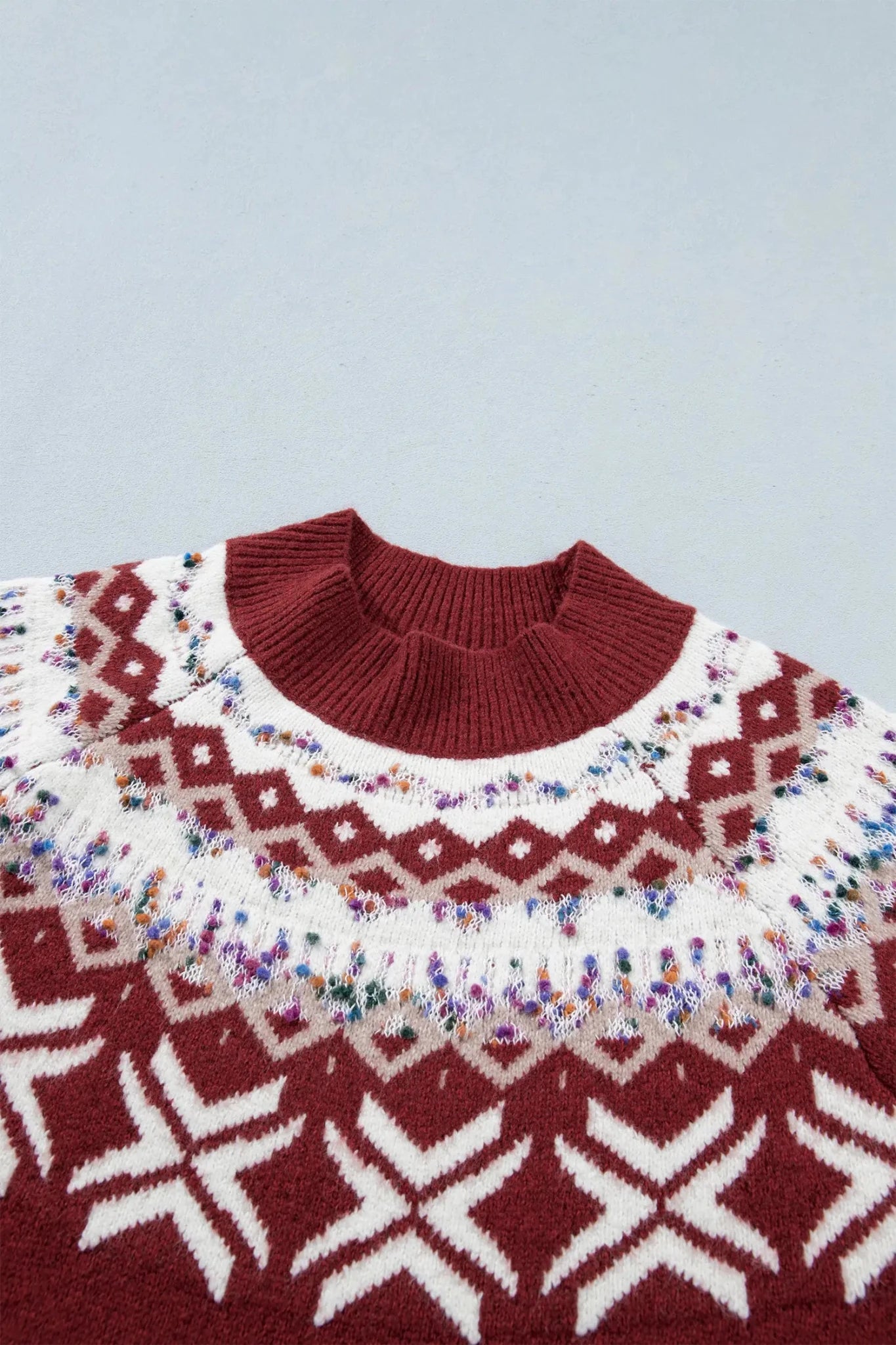 Close-up of a dark red mock-neck sweater with white, beige, and colorful Fair Isle accents.