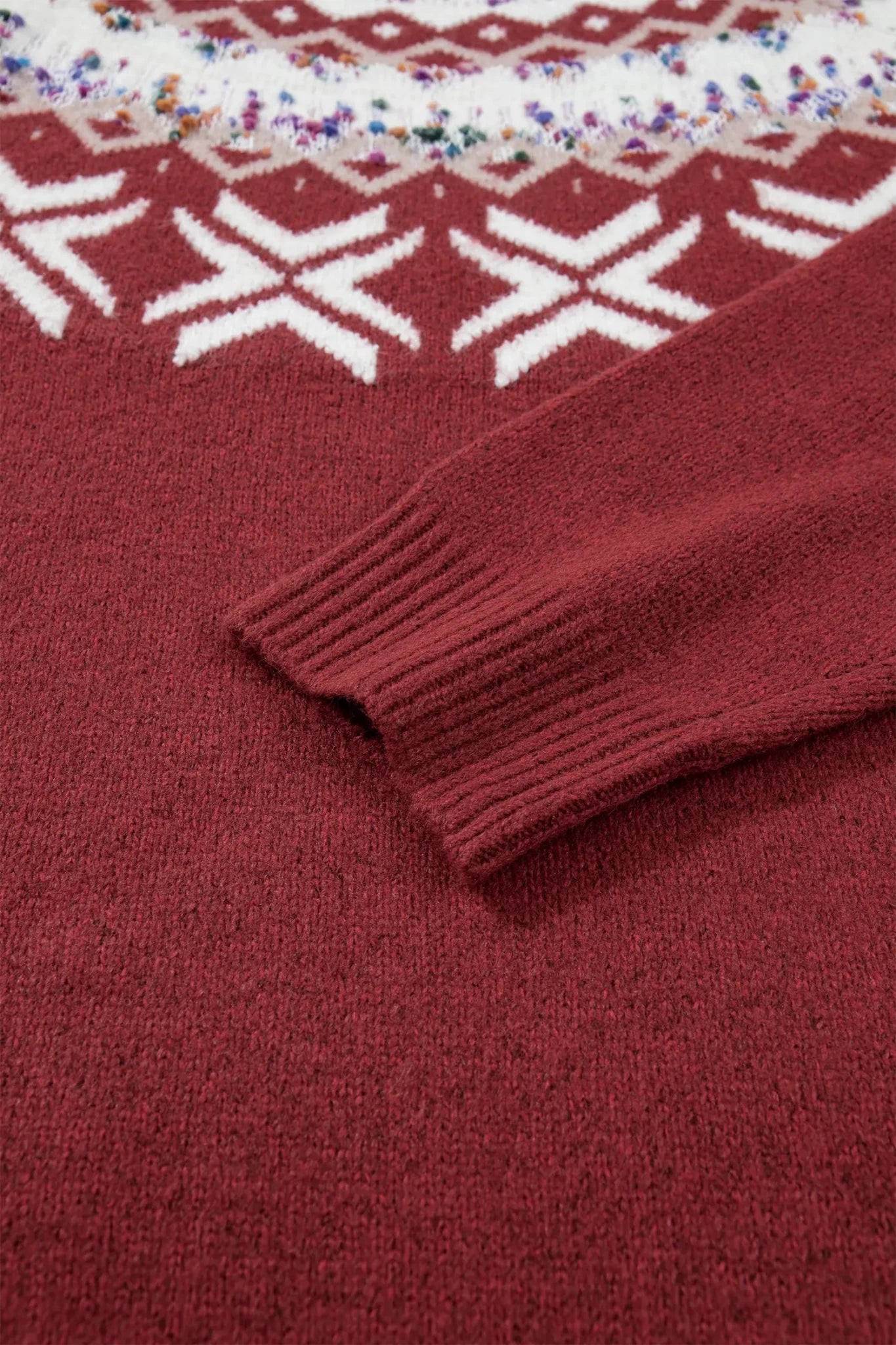 Close-up of a deep burgundy knit sweater with white geometric pattern and ribbed cuff.