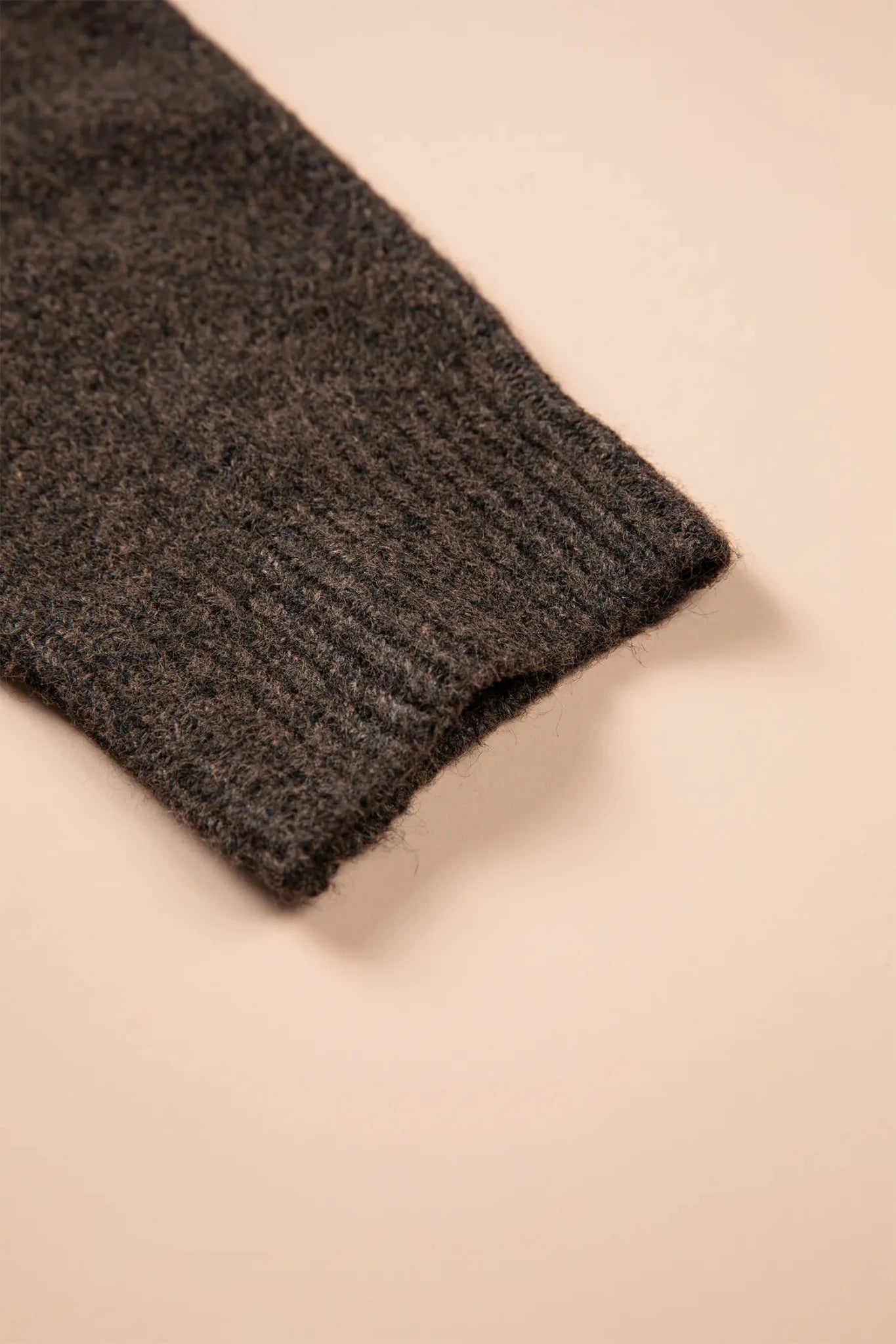 Close-up of a dark charcoal ribbed knit cuff laid diagonally on a beige background.