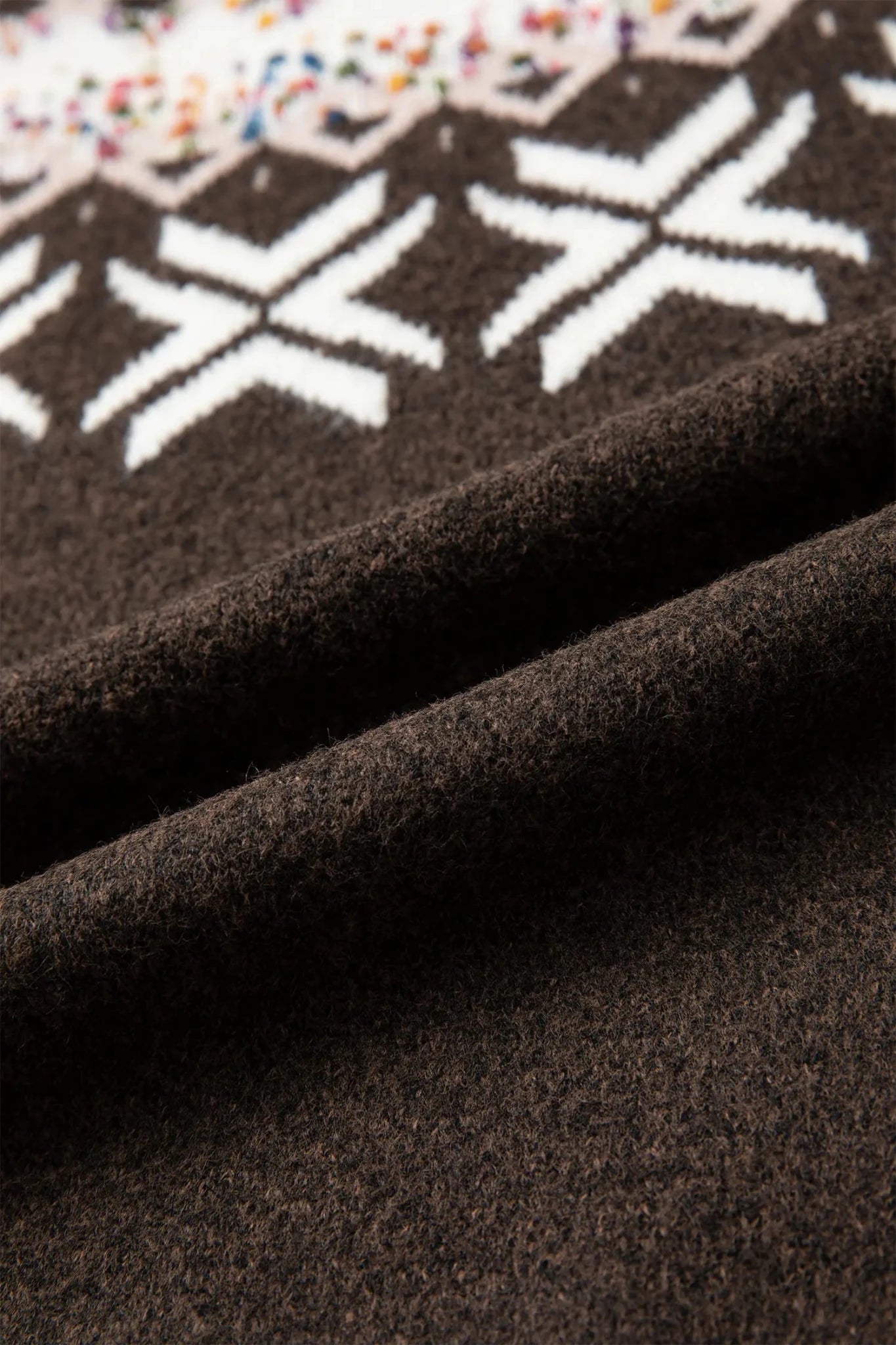 Close-up of dark brown knit fabric with white star patterns and colorful speckled details.