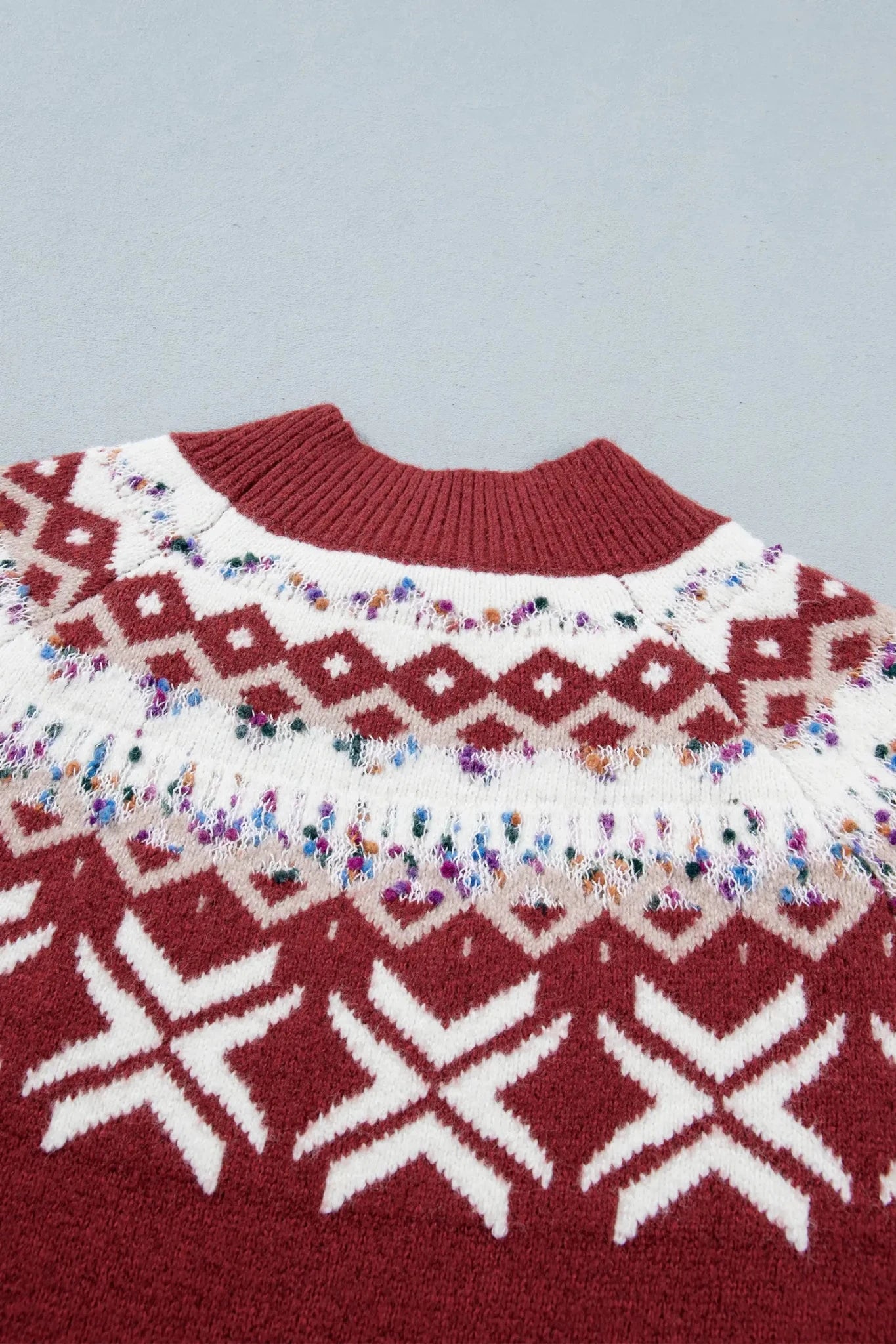 Close-up of a burgundy sweater with a white geometric pattern and colorful speckled band.
