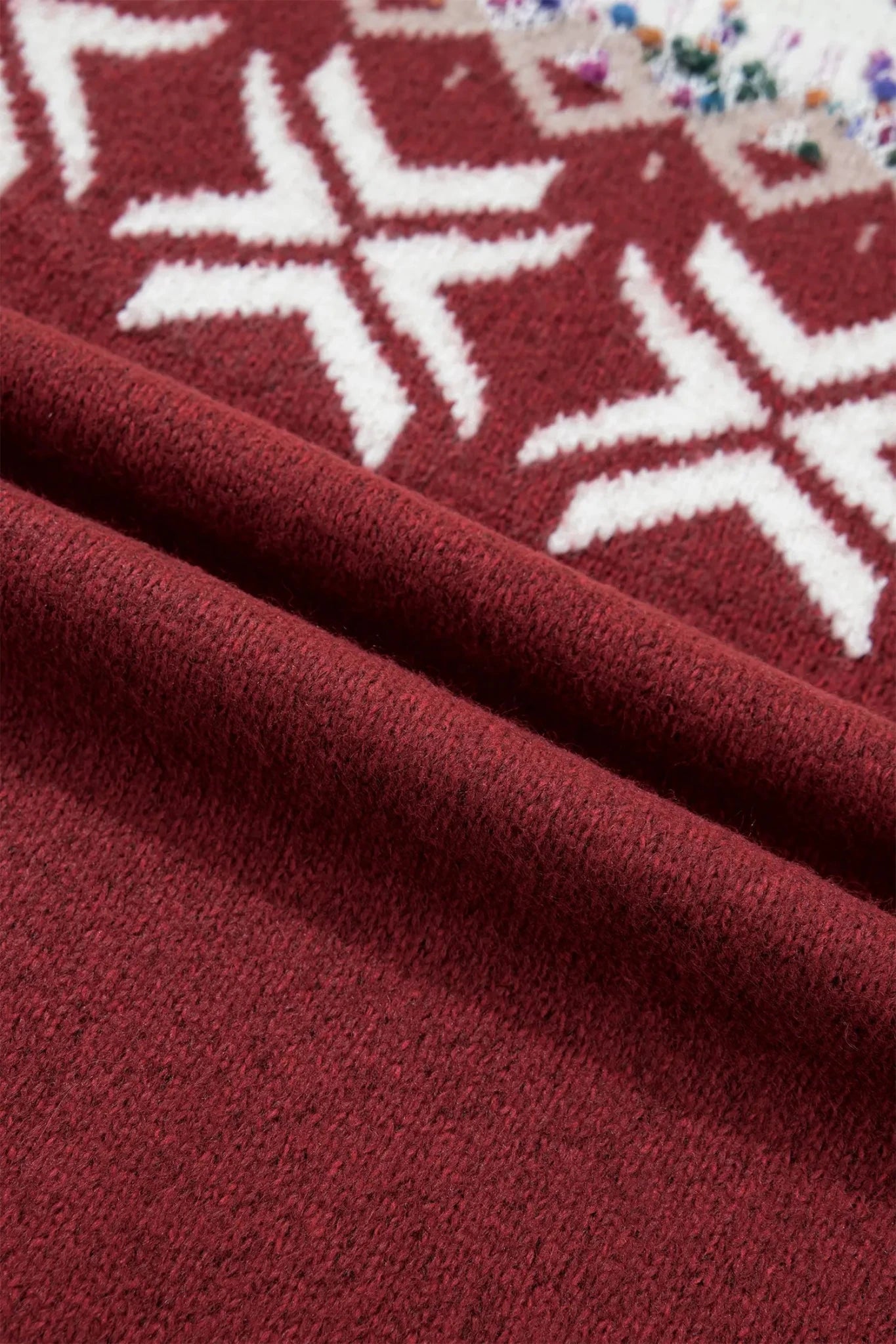 Deep burgundy knit fabric with white snowflake patterns and a small multicolor floral motif.