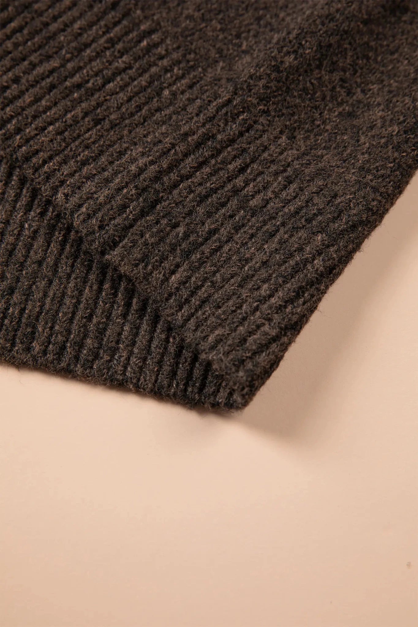 Close-up of dark charcoal gray ribbed knit fabric with a folded edge on beige.