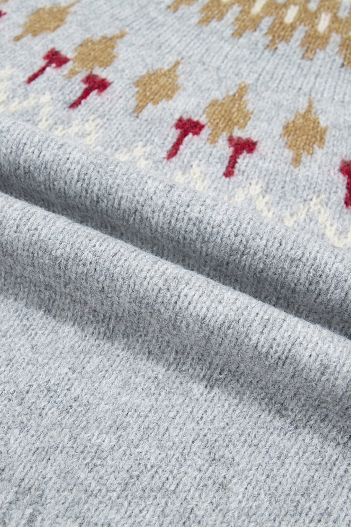 Close-up of light gray knit fabric with tan, red, and off-white Fair Isle motifs.