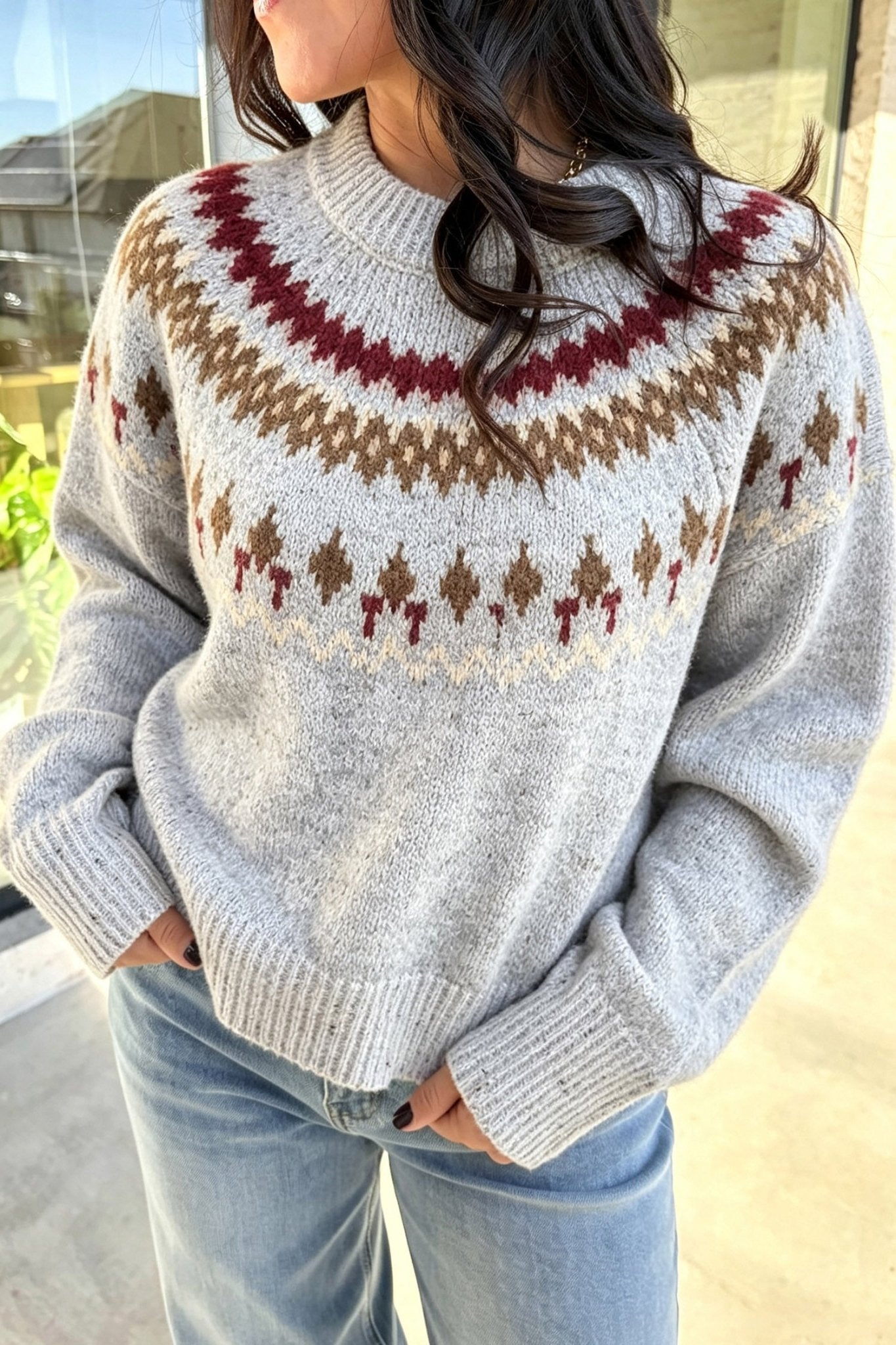 Woman in light gray Fair Isle sweater with brown-burgundy pattern and blue jeans.