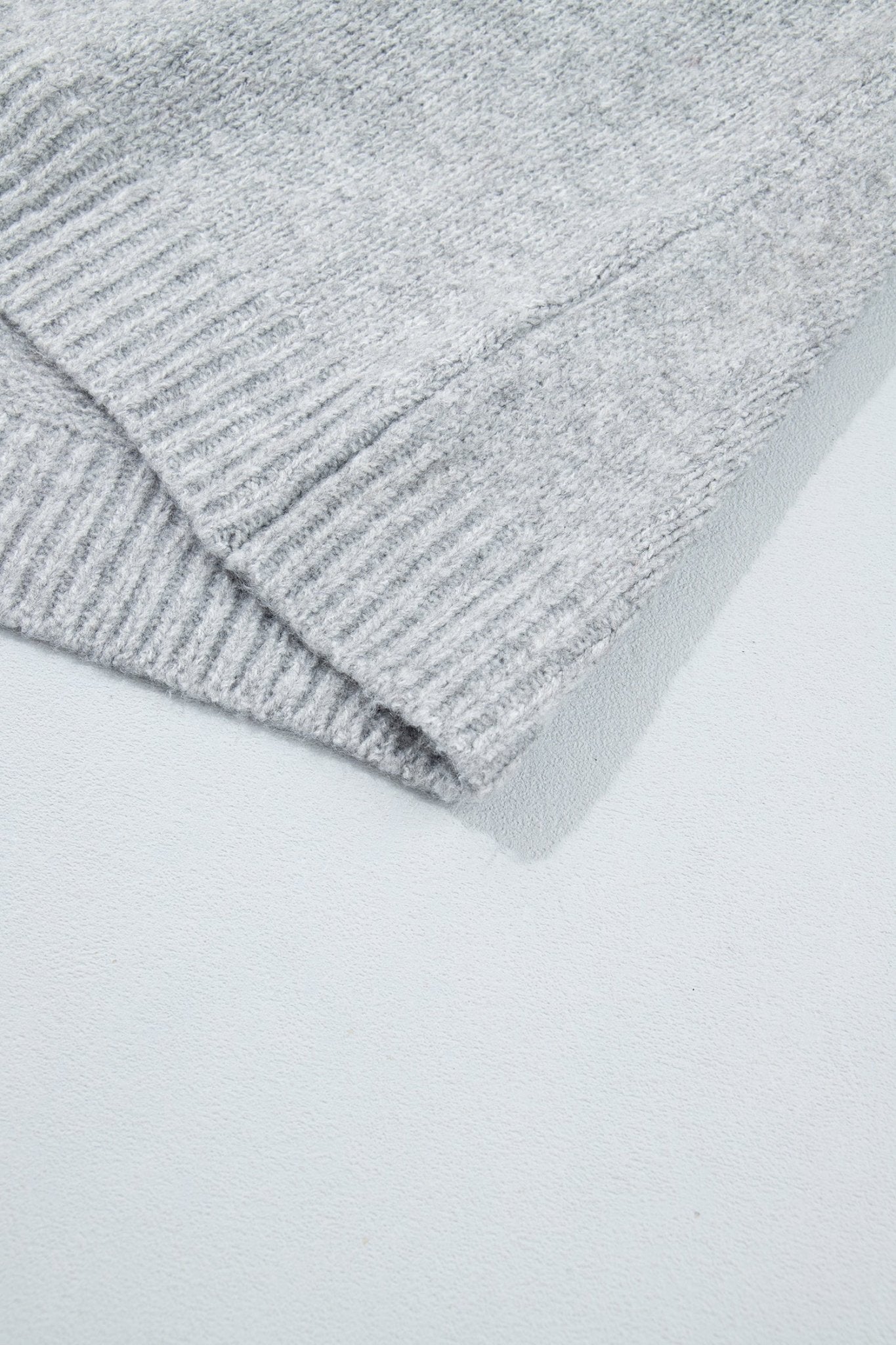 Close-up of light gray ribbed knit fabric with folded edge on white background.