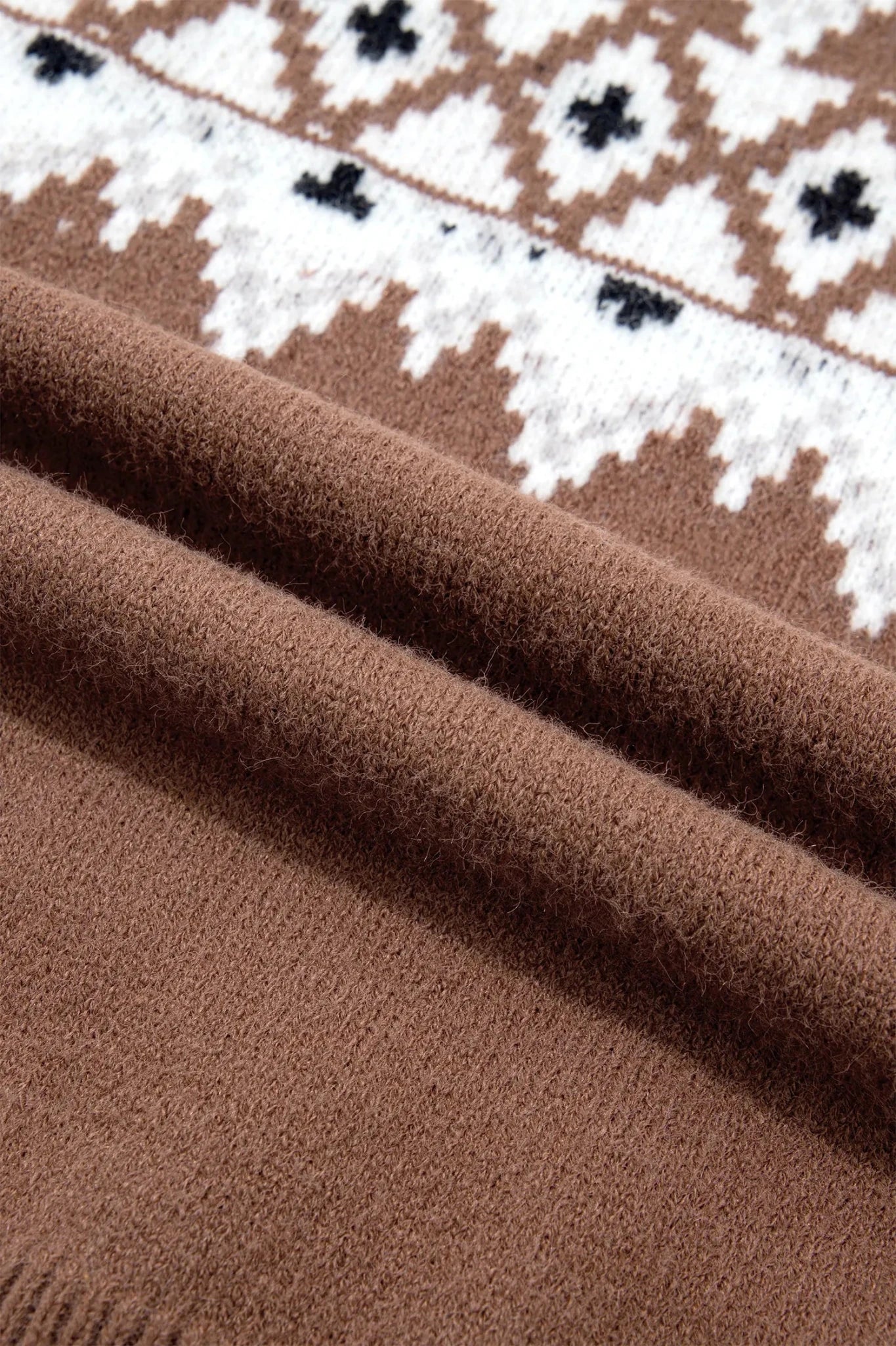 Close-up of brown knit fabric with white and black geometric pattern, showing texture and folds.