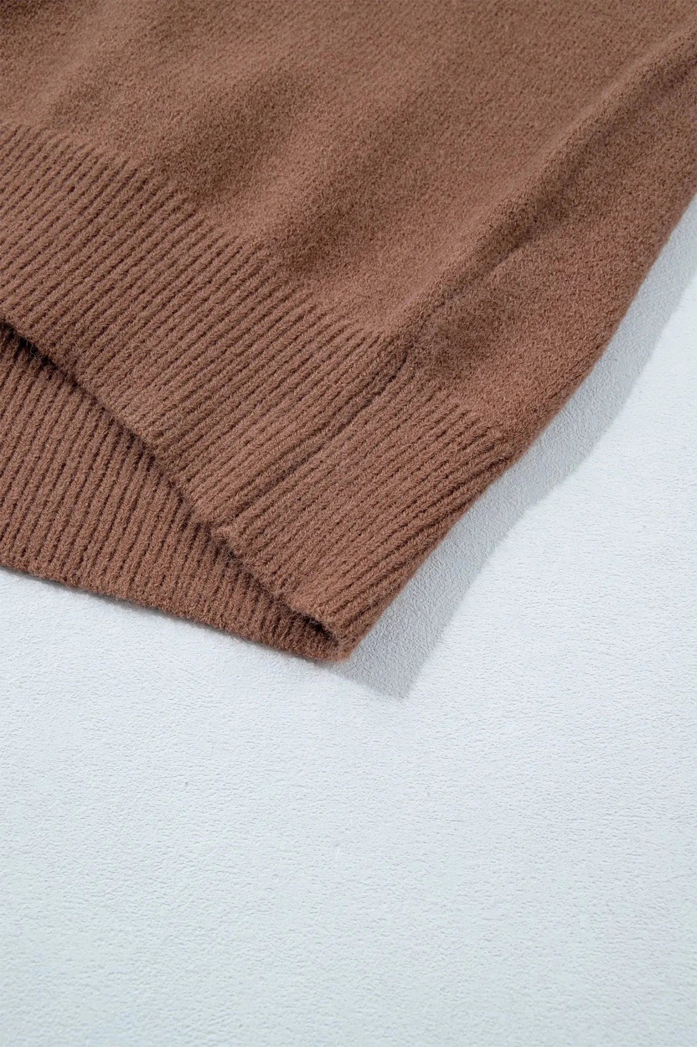 Close-up of a brown ribbed knit fabric corner folded over onto a light gray textured surface.